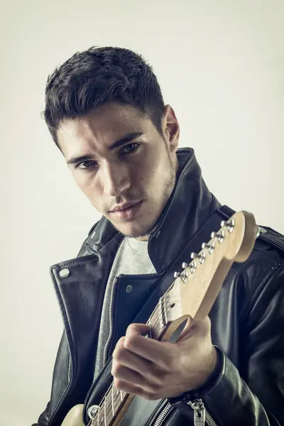 A man in a leather jacket holding a guitar. Photo of a musician rocking out in studio with his guitar
