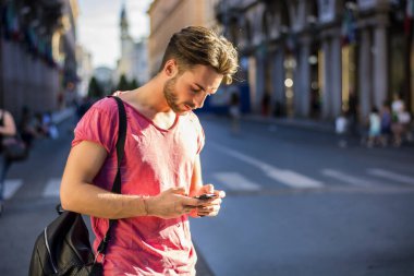 Sokakta durmuş cep telefonuna bakan bir adam. Meşgul bir caddede cep telefonuna takılmış bir adamın fotoğrafı.