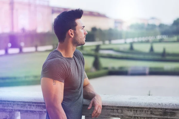 A man leaning on a wall looking off into the distance. Photo of a muscular and attractive man leaning on a wall, lost in thought
