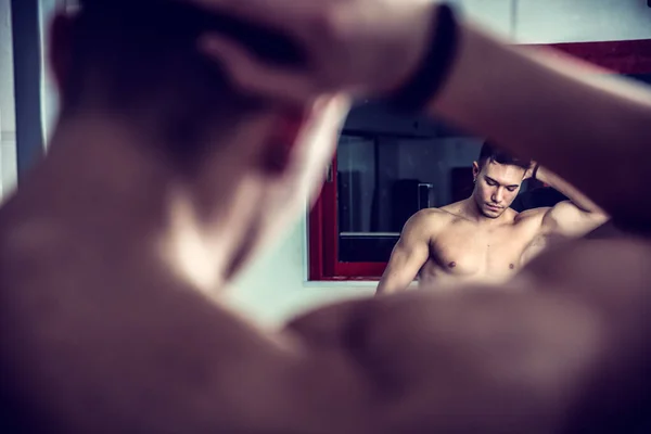 A shirtless young man that is standing in front of a mirror. Photo of a man standing in front of a mirror