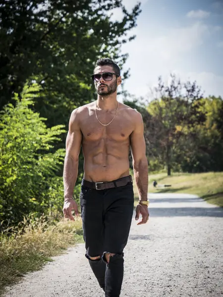 A shirtless man walking down a dirt road. Photo of a shirtless athletic fit man walking down a dirt road