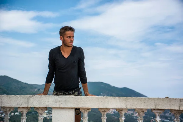 A man standing on a balcony with a mountain in the background. Photo of a man enjoying the breathtaking view of a majestic mountain from a balcony