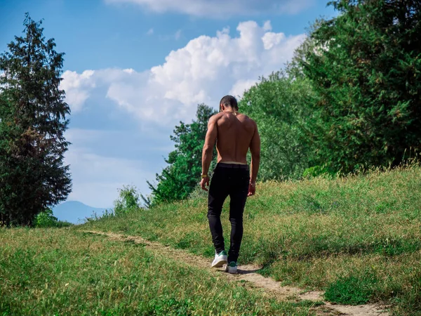 A shirtless man walking down a dirt path. Photo of a shirtless man walking along a rustic dirt path