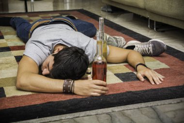 Yerde bir şişe alkolün yanında yatan bir adam. Yerde bir şişe alkolün yanında yatan genç ve yakışıklı bir adamın fotoğrafı.