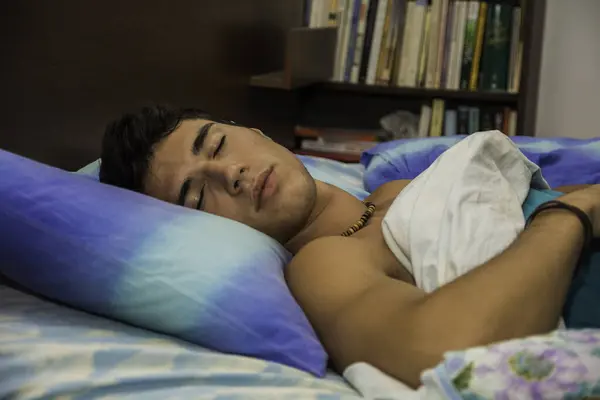 A man laying on a bed with a pillow. Photo of a handsome young man resting on a comfortable bed with a soft pillow