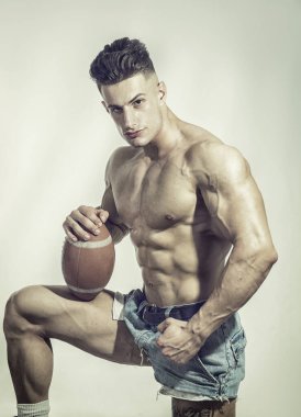 Bir fotoğraf için elinde futbol topu tutan üstsüz bir adam.