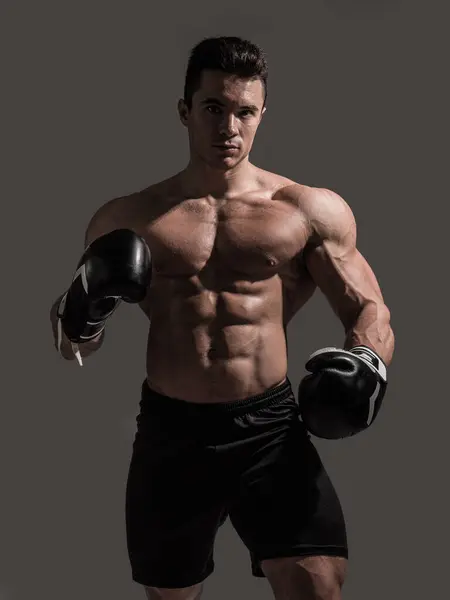A muscular young man in studio with no shirt and boxing gloves