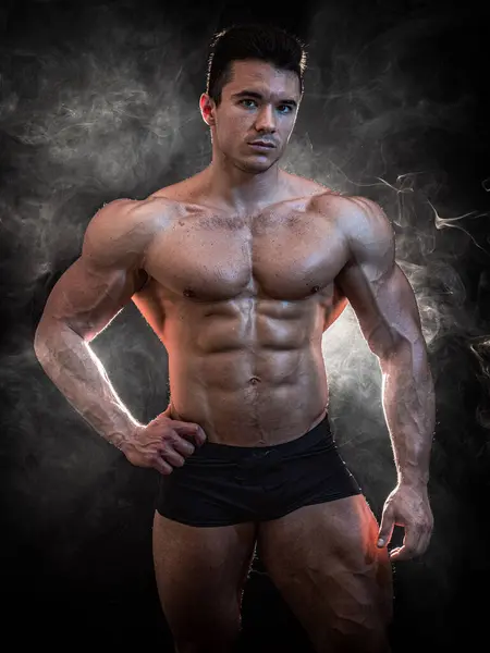 A Strong Display of Masculinity: Flexing Muscles and Striking a Pose in Studio. A man posing for a picture while flexing his muscles in dramatic lights in studio