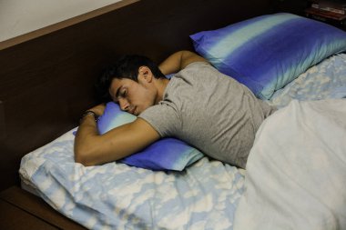 Yastıkla yatakta yatan bir adam. Yumuşak yastıklı, rahat bir yatakta dinlenen yakışıklı bir genç adamın fotoğrafı.