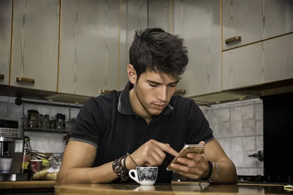 A man sitting at a kitchen counter looking at his cell phone