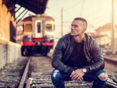 Avrupa 'da şehir merkezinde siyah deri ceket ve kot pantolon giyen yakışıklı bir genç adam.