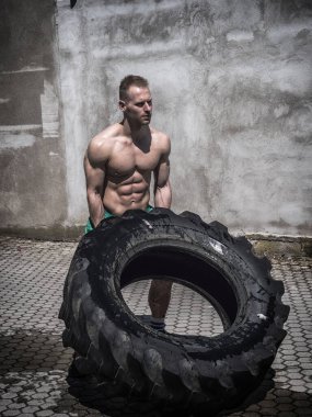 Yakışıklı, kaslı, spor yapan, büyük kamyonet lastiği takla atan genç bir adam.