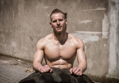 Yakışıklı, kaslı, spor yapan, büyük kamyonet lastiği takla atan genç bir adam.