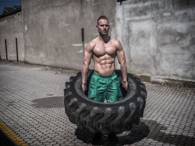 Yakışıklı, kaslı, spor yapan, büyük kamyonet lastiği takla atan genç bir adam.