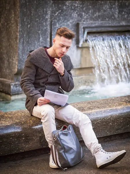 Νεαρός Άνδρας Φοιτητής Που Κάθονται Από Σιντριβάνι Ανάγνωση Φύλλα Χαρτιού Εικόνα Αρχείου