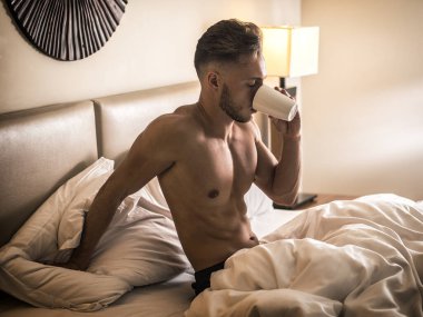 Tamamen çıplak seksi genç adam yatakta kupa veya kahve veya çay yardım kadehte kas vücut ile