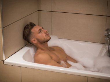 Evde küvet içinde yakışıklı genç adam banyoda, küvet kenar eğilerek,