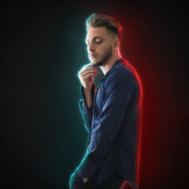 Yakışıklı genç adam stüdyo çekimlerinde aşağı bakıyor, koyu arkaplanda, çift ışık efektli.