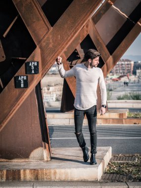Şehirdeki yakışıklı bir adam Avrupa 'da paslı bir metal yapının yanında oturuyor ve başka tarafa bakıyor.