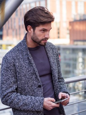 Trendy yakışıklı cardingan ayakta ve cep telefonuyla, açık şehir ayarında gün atış yazarak