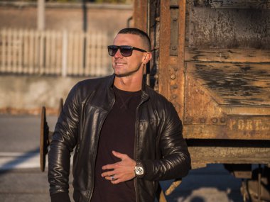 Avrupa 'da şehir merkezinde siyah deri ceket ve kot pantolon giyen yakışıklı bir genç adam.