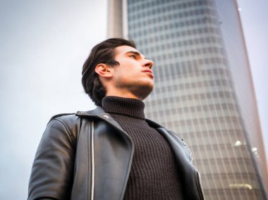 Modern şehirde yakışıklı bir genç adam, siyah deri ceket ve kot pantolon giyiyor.