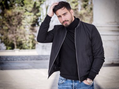 Modern şehirde oturan, siyah deri ceket ve kot pantolon giyen yakışıklı bir genç.