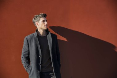 Ciddi yakışıklı delikanlı kış kıyafeti büyük boşaltmak çerçevenin bir tarafa bakarken kırmızı Metal duvara yaslanmış