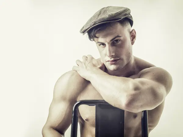 Μυώδης Bodybuilder Κάθεται Στην Καρέκλα Κοιτάζοντας Κάμερα Φορώντας Καπέλο Φωτογραφία Αρχείου