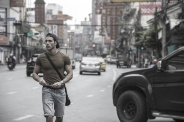 Muscular young handsome man walking on busy sunny street in Bangkok, Thailand.