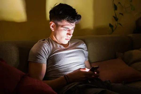 남자가 소파에 휴대전화 화면에 앉아있습니다 스크롤하고 장치와 작용으로 나타납니다 메시지 스톡 이미지