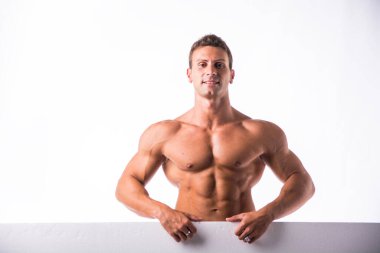 Üstsüz bir adam kameranın önünde duruyor ve fotoğraf için poz veriyor. Kaslı vücudunu gururla sergiliyor..