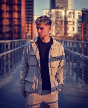 Bir adam köprüde duruyor ve hareketli bir şehre bakıyor. Arka planda binalar ve şehir trafiğiyle ufuk çizgisine bakıyor. Sahne şehir ortamını yakalar ve insanlar düşüncelere dalarlar..