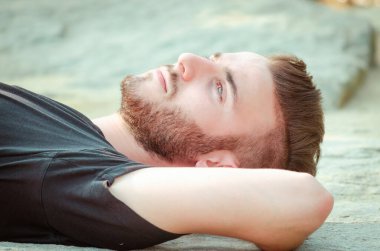 Genç bir adam kayalık bir yüzeyde uzanmış güneşin sıcaklığının tadını çıkarıyor. Sakin bir ifadeyle yukarıya bakıyor. Huzur ve huzur dolu bir anı yansıtıyor..