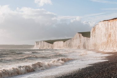 Seven Sisters tebeşir kayalıklarının oradaki çakıl taşlı sahile vuran dalgalar, doğu Sussex, İngiltere 'nin güney kıyısındaki en uzun gelişmemiş kıyı şeritlerinden biri..