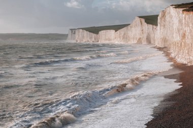 Seven Sisters tebeşir kayalıklarının oradaki çakıl taşlı sahile vuran dalgalar güney sahilinin en uzun ve gelişmemiş kıyı şeritlerinden biri olan Doğu Sussex, İngiltere 'de..