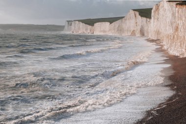 Seven Sisters tebeşir kayalıklarının yanındaki sahile vuran dalgalar güney kıyısındaki en uzun gelişmemiş kıyı şeritlerinden biri, Doğu Sussex, İngiltere.