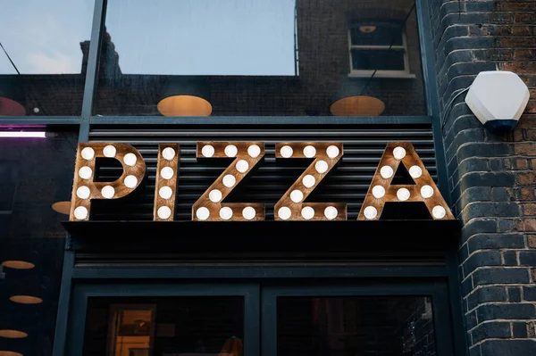 Pizza light bulb illuminated sign outside a restaurant in East London, UK.