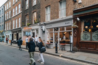 Londra, İngiltere - 13 Nisan 2023: Londra 'nın LGBTQ + barları, restoranları ve kulüpleri ile ünlü bir bölgesi olan Soho' daki restoranların sıralanması, insanların geçişi, seçici odak noktası.