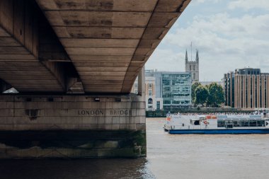 Londra, İngiltere - 06 Temmuz 2023: Thames Nehri üzerinde Londra Köprüsü 'nü geçen tekne. Nehir turları tüm yıl boyunca turistler arasında çok popülerdir..