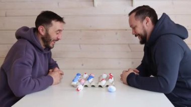 Sakallı adamlar beyaz masada Paskalya yumurtalarıyla satranç oynarlar. Alışılmadık satranç için yaratıcı fikirler. Renkli yumurta figürleri. Yüksek kalite 4k görüntü