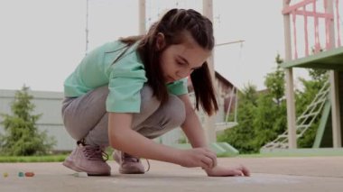 Kız asfalta renkli pastel boyalarla resim çiziyor. Duvarında tebeşir olan çocuk çizimleri. Yaratıcı çocuk. Çocukluk sevinci. Yüksek kalite 4k görüntü