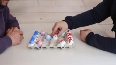 İki adam beyaz masada Paskalya yumurtalarıyla satranç oynuyor. Alışılmadık satranç için yaratıcı fikirler. Renkli yumurta figürleri. Yüksek kalite 4k görüntü