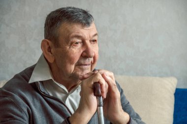 Gri arka planda üzgün yaşlı bir adamın portresi. Evde tek başına oturan yaşlı ihtiyarın düşünceli bakışları. Kırışık yüzün yakın çekimi, kopyalama alanı. Yüksek kalite fotoğraf