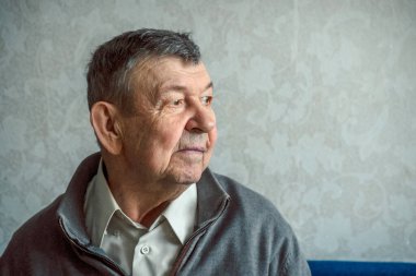 Gri arka planda üzgün yaşlı bir adamın portresi. Evde tek başına oturan yaşlı ihtiyarın düşünceli bakışları. Kırışık yüzün yakın çekimi, kopyalama alanı. Yüksek kalite fotoğraf