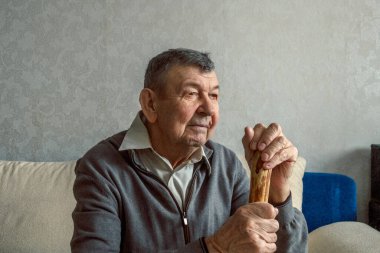 Gri arka planda üzgün yaşlı bir adamın portresi. Evde tek başına oturan yaşlı ihtiyarın düşünceli bakışları. Kırışık yüzün yakın çekimi, kopyalama alanı. Yüksek kalite fotoğraf