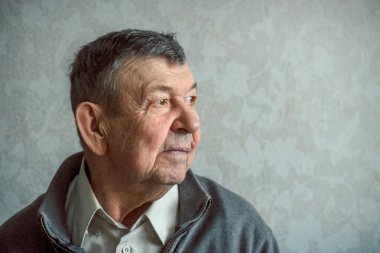 Gri arka planda üzgün yaşlı bir adamın portresi. Evde tek başına oturan yaşlı ihtiyarın düşünceli bakışları. Kırışık yüzün yakın çekimi, kopyalama alanı. Yüksek kalite fotoğraf