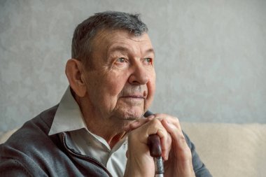 Gri arka planda üzgün yaşlı bir adamın portresi. Evde tek başına oturan yaşlı ihtiyarın düşünceli bakışları. Kırışık yüzün yakın çekimi, kopyalama alanı. Yüksek kalite fotoğraf