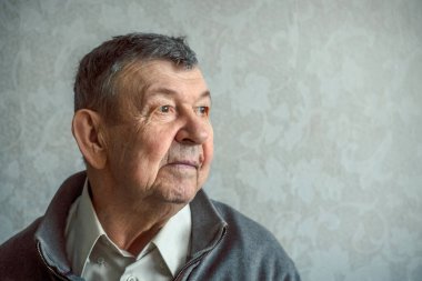 Gri arka planda üzgün yaşlı bir adamın portresi. Evde tek başına oturan yaşlı ihtiyarın düşünceli bakışları. Kırışık yüzün yakın çekimi, kopyalama alanı. Yüksek kalite fotoğraf