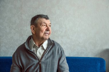 Gri arka planda üzgün yaşlı bir adamın portresi. Evde tek başına oturan yaşlı ihtiyarın düşünceli bakışları. Kırışık yüzün yakın çekimi, kopyalama alanı. Yüksek kalite fotoğraf